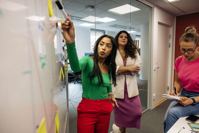 Businesswoman planning strategy with colleagues over whiteboard at office