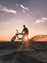 Silhouette man riding bicycle on street during sunset