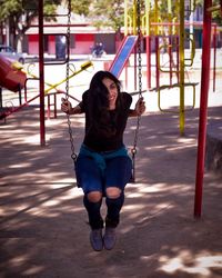 Portrait of smiling young woman sitting on swing at playground