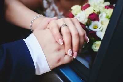 Cropped image of bride holding hands of groom while sitting in car