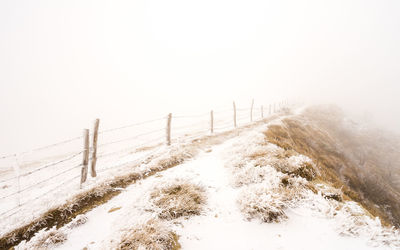 Snow covered fence against sky during winter