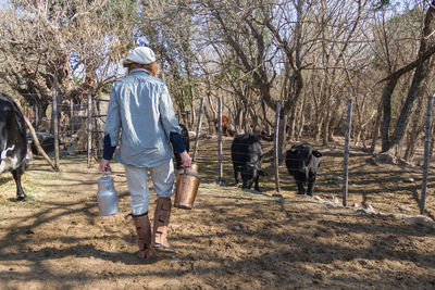 Rear view of woman holding containers walking on farm against trees