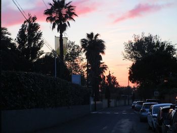 Road by silhouette trees against sky during sunset