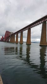 Low angle view of bridge over river against cloudy sky