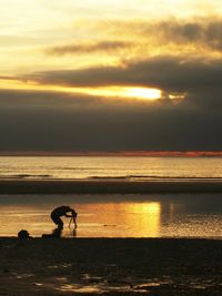 Silhouette man by sea against sky during sunset