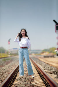 Smiling girl standing on railroad track against clear sky