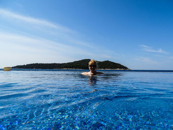 Woman swimming in infinity pool against blue sky