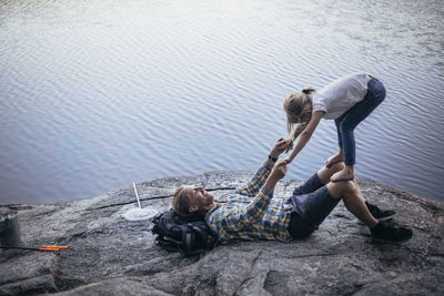 Smiling father playing with daughter while lying down by lake