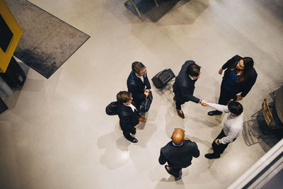 High angle view of colleague standing with businessmen shaking hands at office