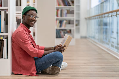 Smiling black student man reading book in university library , looking at camera. reading hobby.