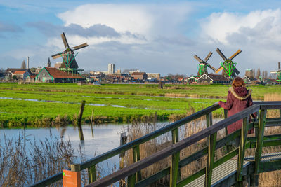 Rear view of woman standing by field on footbridge