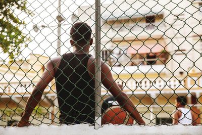 Rear view of woman sitting by chainlink fence