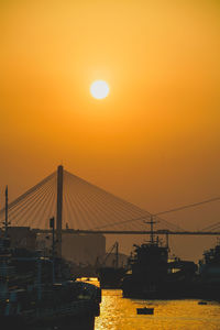 Silhouette bridge over sea against sky during sunset