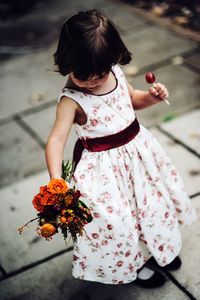 Cute girl holding bouquet and candy on footpath