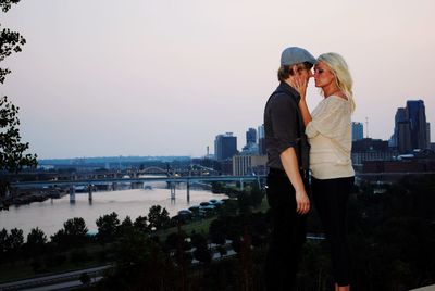 Side view of couple romancing on building terrace by river in city