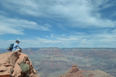 Rear view of man sitting on rock against sky