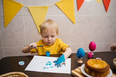 Child draws on paper with paint, paints easter eggs