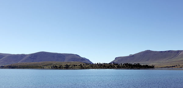 Scenic view of lake and mountains against clear blue sky