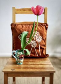 Close-up of single pink tulip in vintage vase on wooden chair with brown, embroidered cushion 