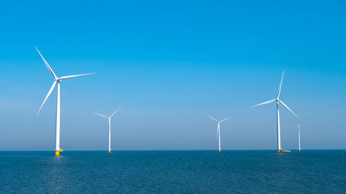 Windmills on field against clear blue sky