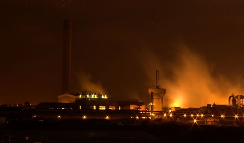 Illuminated factory against sky at night