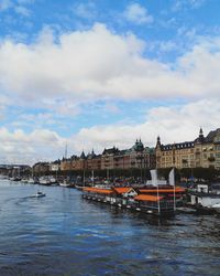 View of buildings by river against cloudy sky