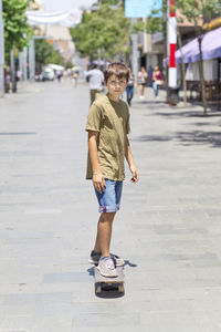 Full length of boy skateboarding on footpath in city