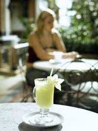 Close-up of drink on against defocused woman at sidewalk cafe