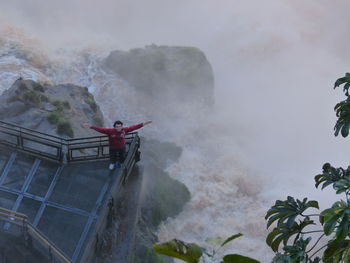 High angle view of man with arms outstretched by iguacu falls