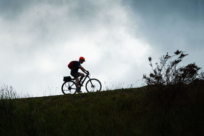 Man riding bicycle on field against sky