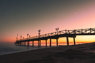 Silhouette pier over sea against sky during sunset