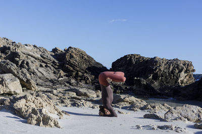 Rear view of woman sitting on rock against clear blue sky