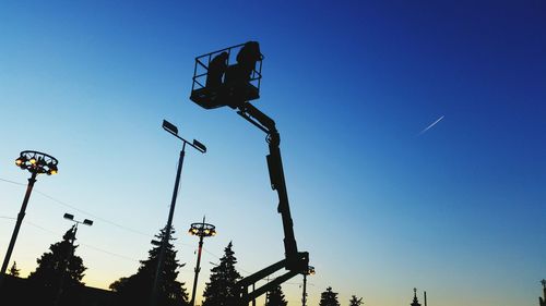 Low angle view of silhouette cherry picker against clear blue sky