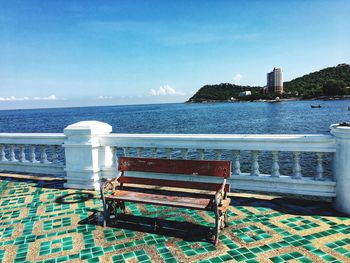 Empty bench by sea against sky