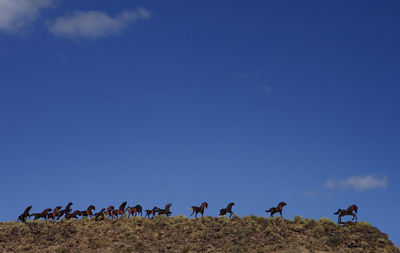 Low angle view of horse statues on hill against blue sky