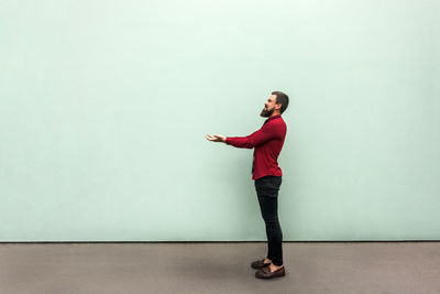 Young man looking away while standing against wall