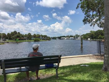 Rear view of man sitting on riverbank against sky