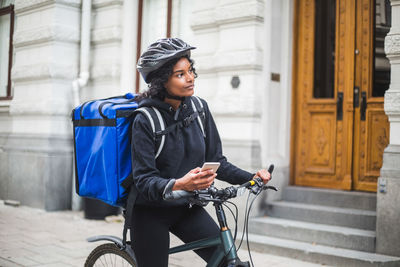 Food delivery woman looking away while holding smart phone in city