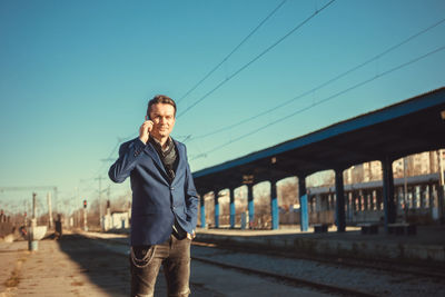 Portrait of man talking on mobile phone against clear sky