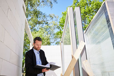 Low angle view of architect reading document while standing at construction site