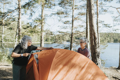 Two senior women setting up tent at campsite at lakeshore