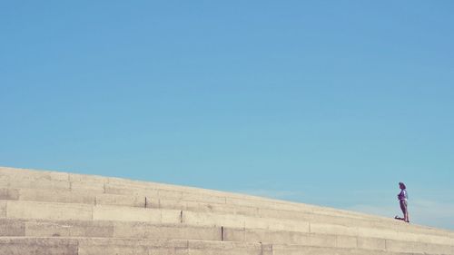 Low angle view of woman standing against clear blue sky