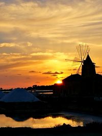 Silhouette traditional windmill by lake against orange sky