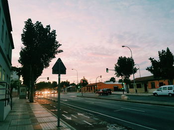 Road by trees against sky during sunset in city