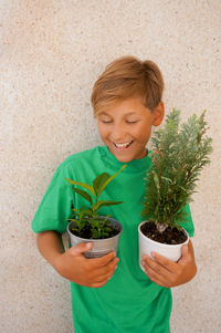Smiling child holding green plant in pot grey background 
