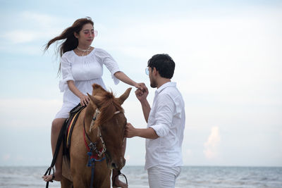 Young woman with boyfriend riding horse at beach