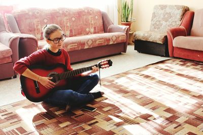 Full length of teenage girl playing guitar while sitting on carpet at home