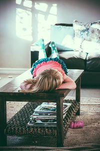 Full length of girl lying on coffee table at home
