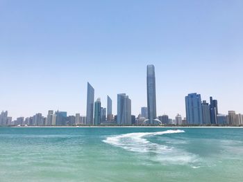 Sea by modern buildings against clear sky