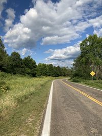 Empty road amidst field against sky